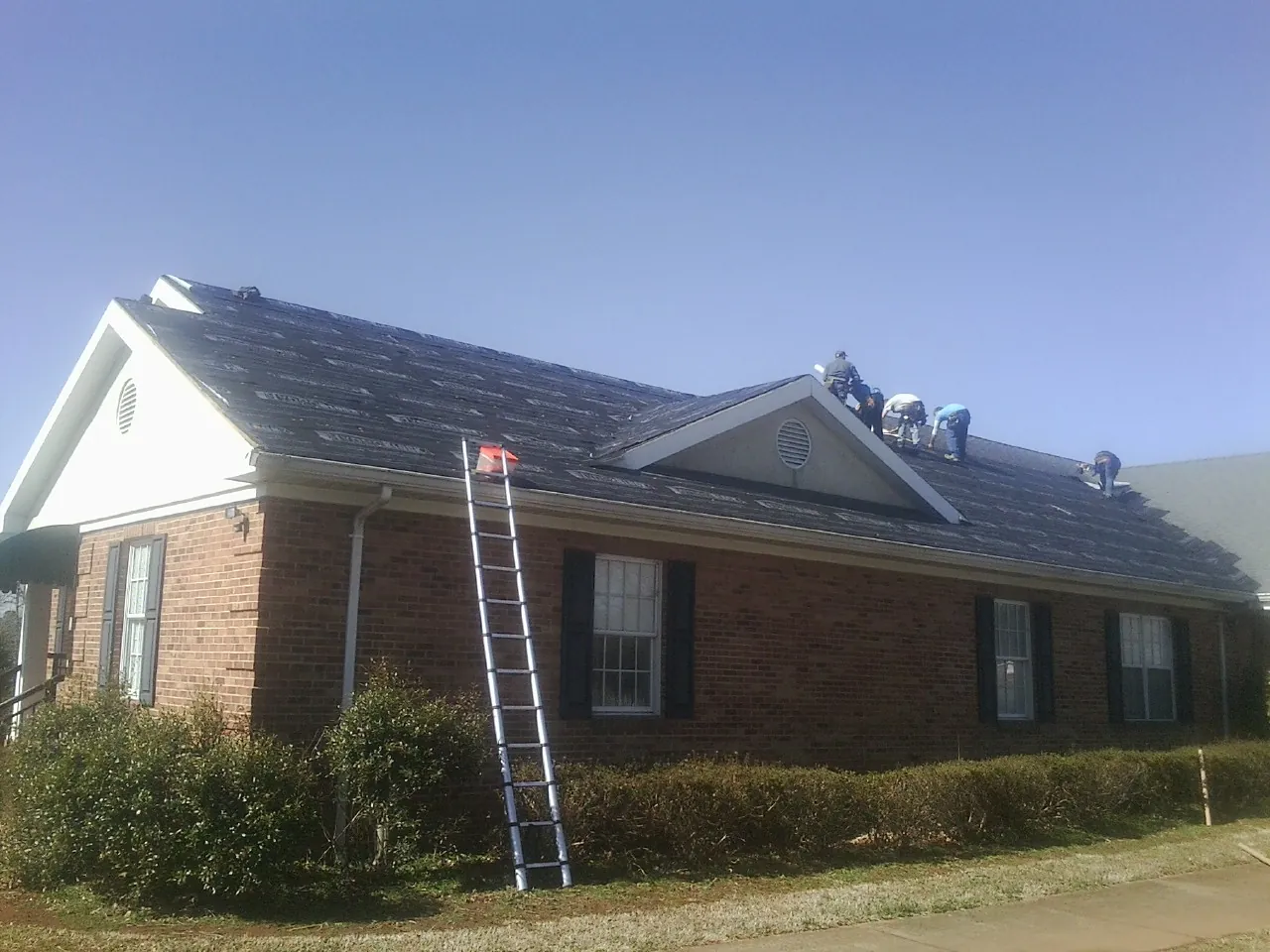 Crew tearing shingles off a brick ranch roof with a ladder set — Emergency Roof Repair work by our crew in Austell