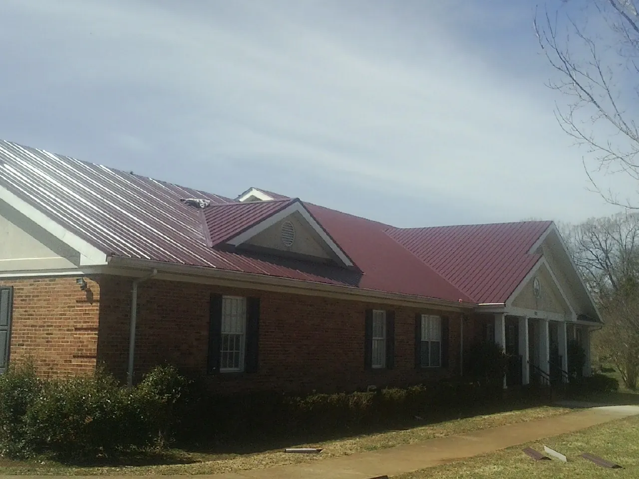 Red metal roof with gabled entries on a long brick building, from a Hail Damage Roof Repair job in Austell