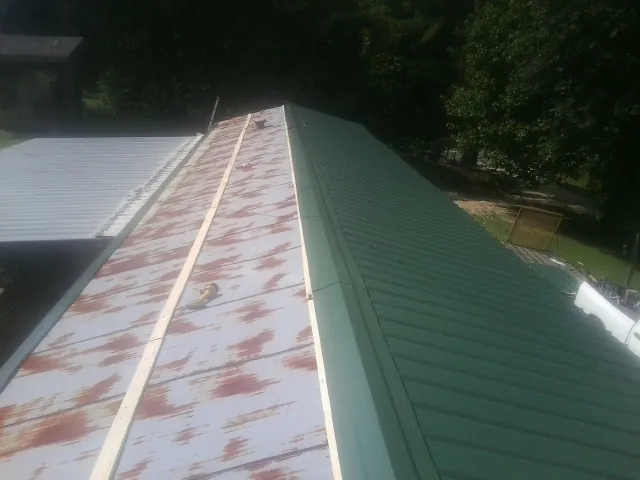 Old rusted panels beside newly installed green metal roofing — Wind Damage Roof Repair by Roofing Brothers in Austell