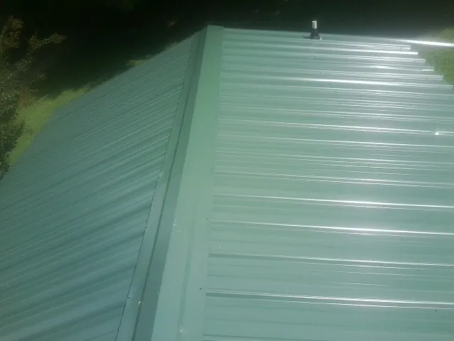 New green metal panels meeting at the ridge of a roof — Flat Roof Repair work by our crew in Austell
