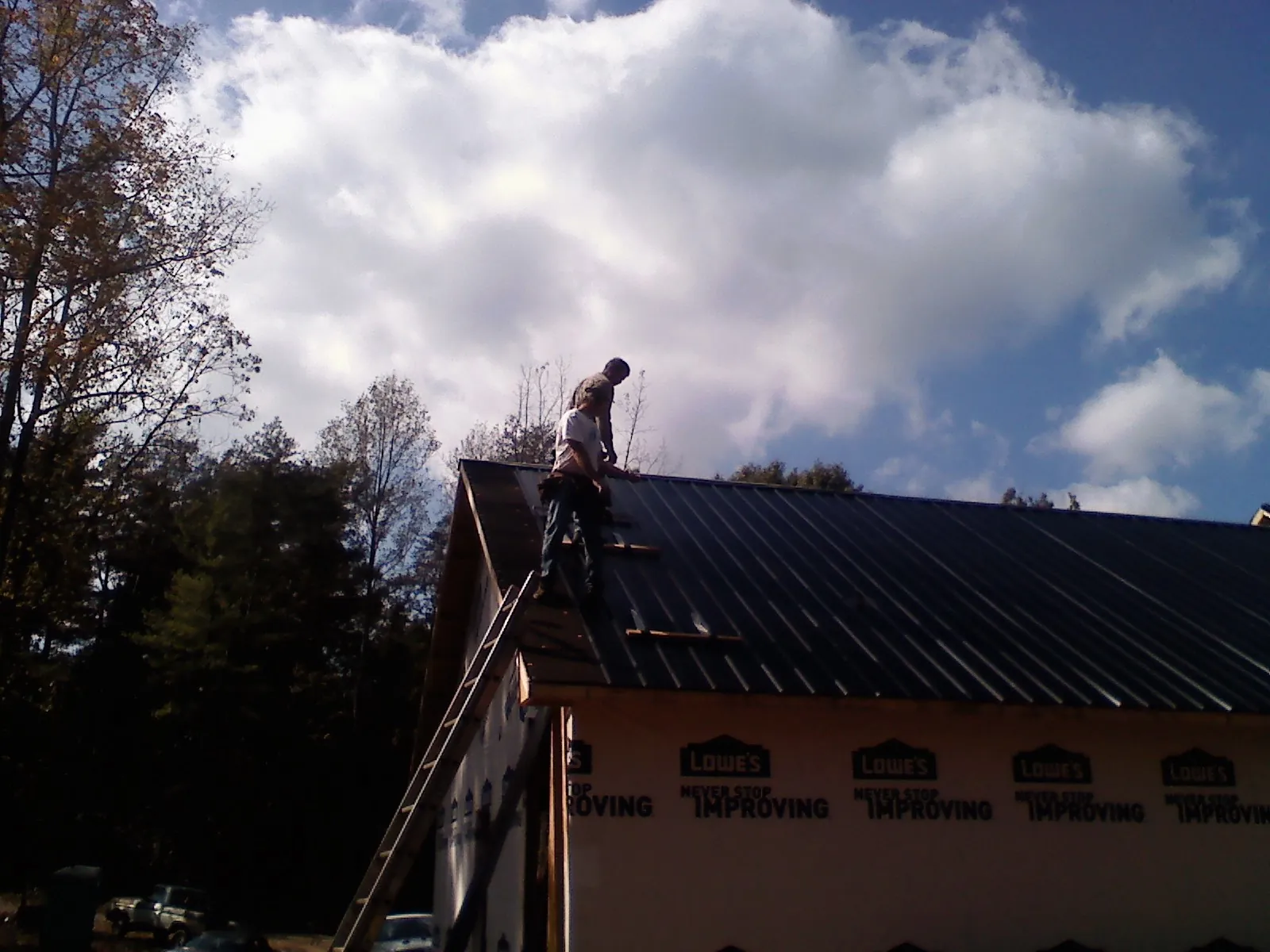 Roofer fastening dark metal panels high against a cloudy sky, from a Roof Inspection job in Austell