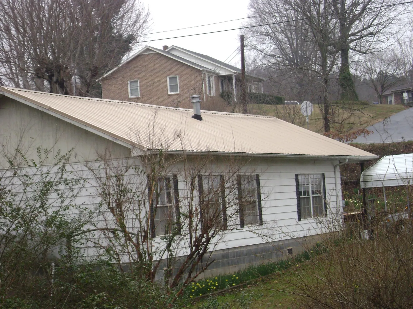 Tan metal roof on a white sided house set into a hillside — Commercial Roofing by Roofing Brothers in Austell